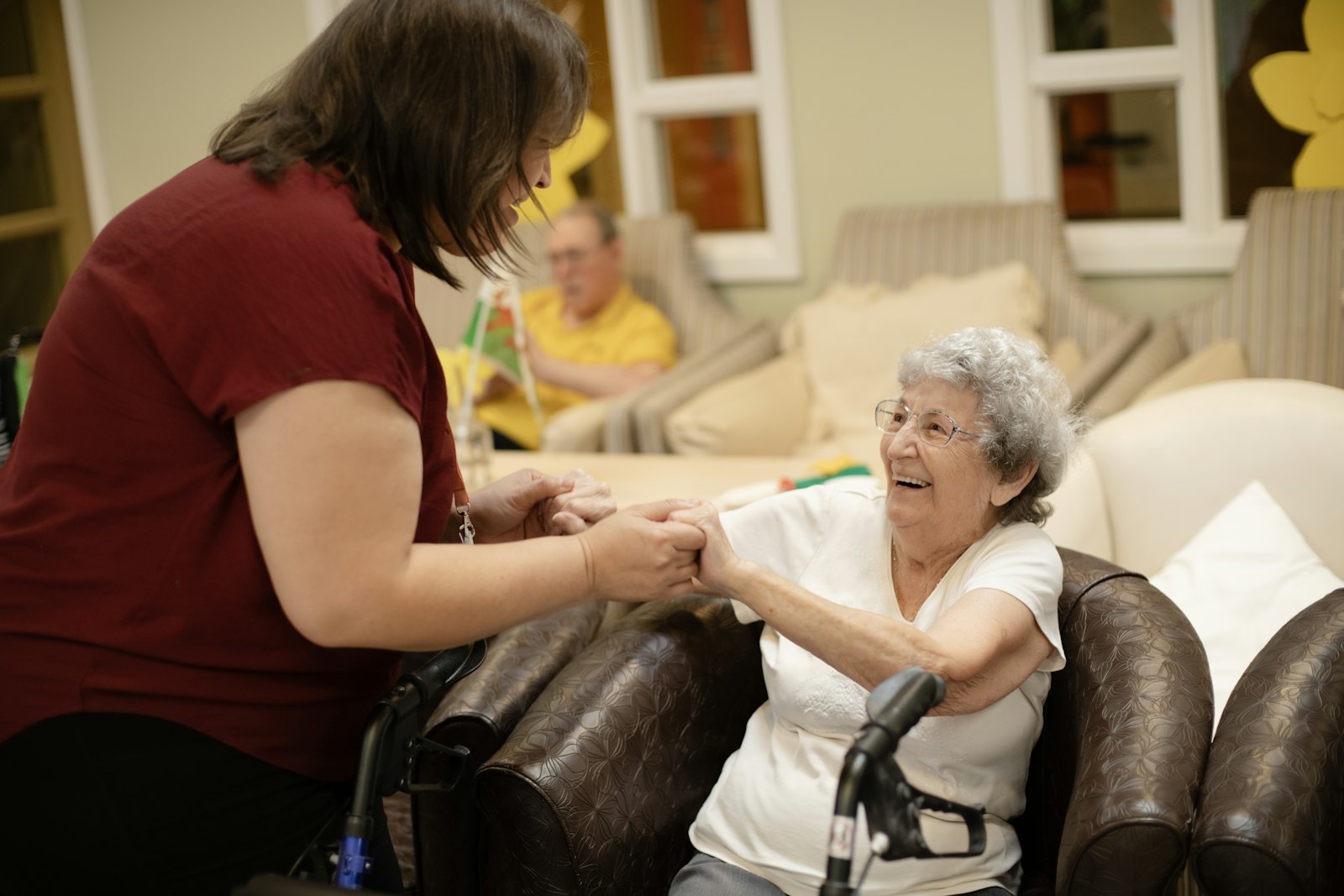 A caregiver holding the hands of a smiling elderly woman